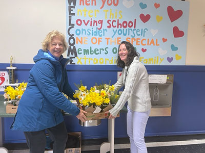 Two women smiling at the camera as one gives the other flowers to be distributed to teachers at the school