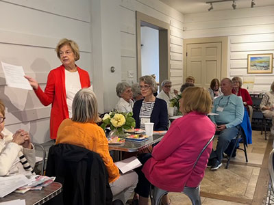 A woman standing and address a group of garden club members seated at tables